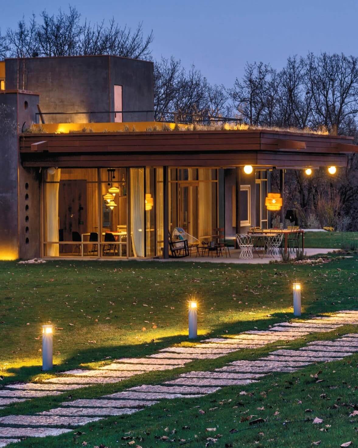 Moderne Architektur mit Platek-Pollerleuchten entlang eines beleuchteten Gartenwegs in der Abenddämmerung